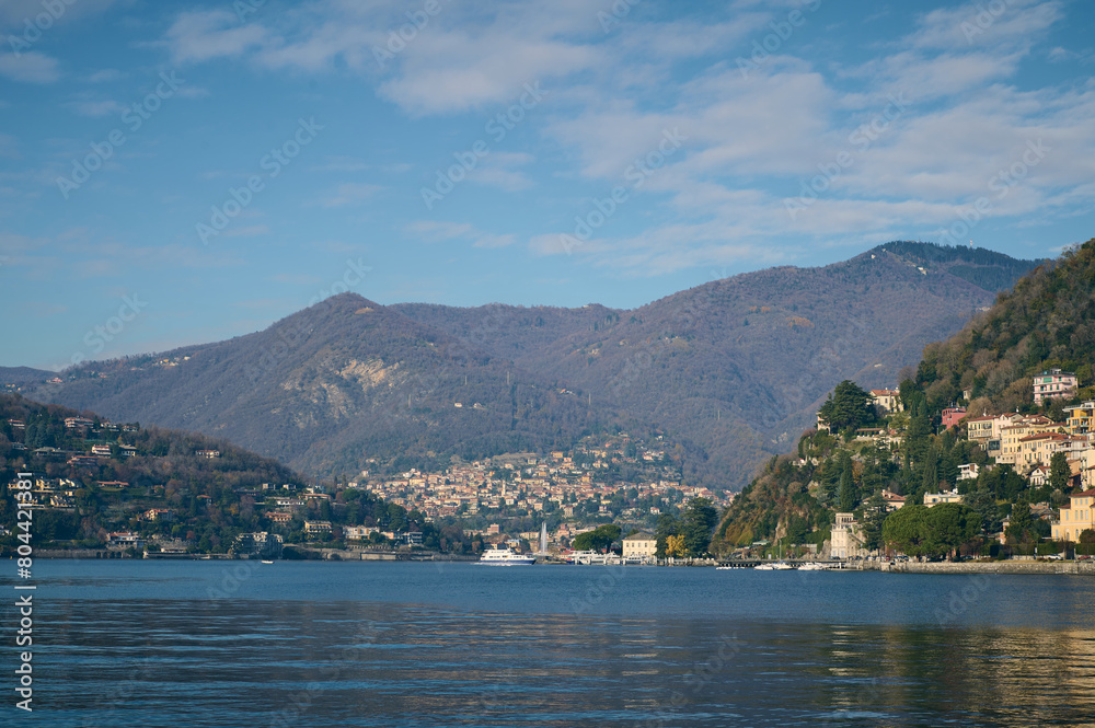 Mesmerizing view of the lake of Como over Alpine mountains background. Clear water of the lake reflecting floating boats and houses on the waterfront. Italy. Nature background, Tourism and travel. Mesmerizing view of the lake of Como over Alpine mountains background. Clear water of the lake reflecting floating boats and houses on the waterfront. Italy. Nature background, Tourism and travel.