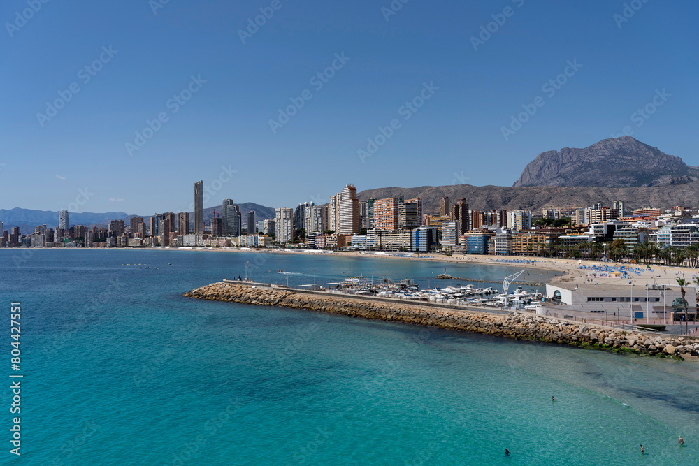 Panorama of Benidorm including the breakwater, small marina, local beach and the majestic Puig Campana mountain in the background.