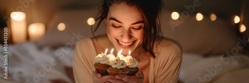 Sincere smile of a woman holding a cupcake with three candles in her hands