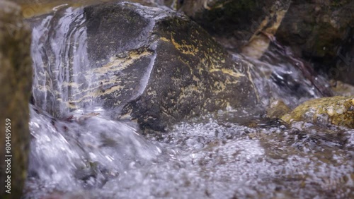 Stream of natural water, flowing on the rocks. Waterfall in the mountains. Close up of the outdoors. This pure liquid stones.