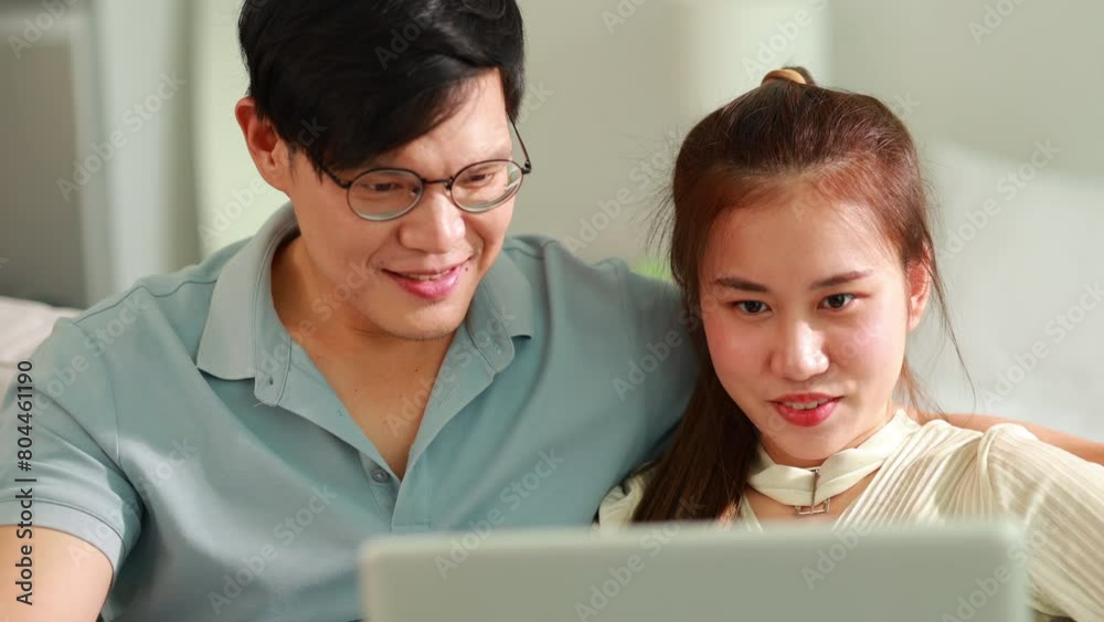 Happy Asian couple with laptop spending time together at home. young couple relax on sofa in living room watch video on laptop together Happy Asian couple with laptop spending time together at home. young couple relax on sofa in living room watch video on laptop together