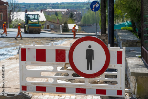 Prohibition of Pedestrian Traffic - road sign at the road construction site.Barriers on the sidewalk of a road under construction, construction machines (road roller and asphalt machine) and workers .