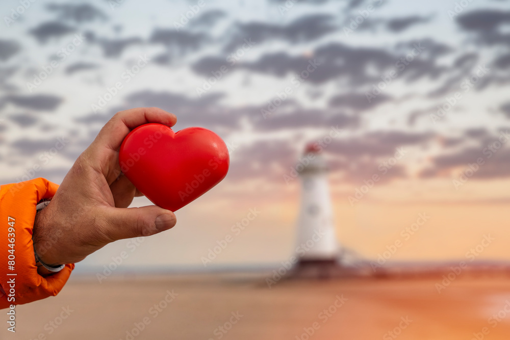 red heart in hand against lighthouse. Fall in love with holiday at seaside concept red heart in hand against lighthouse. Fall in love with holiday at seaside concept