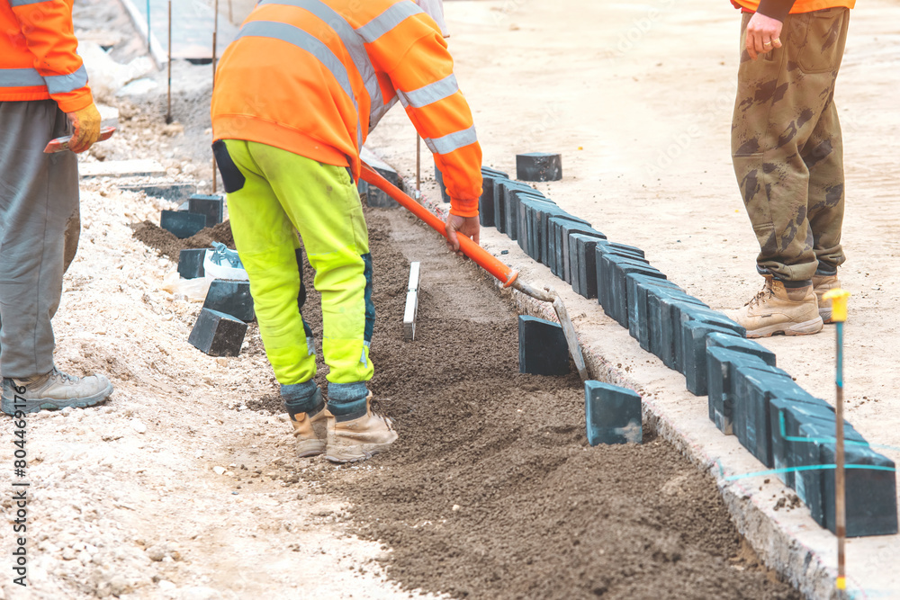 Groundworkers  in hi-viz using shovel leveling concrete  kerbs on  construction site