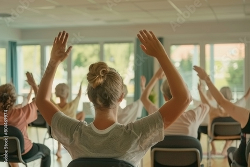 A group of people are in a yoga class, all of them elderly ladies with their hands up in the air