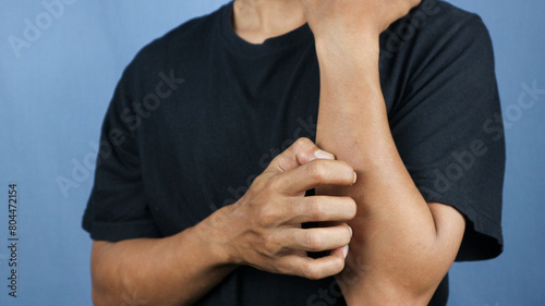 Asian young man scratching his hand isolated on blue background. photo