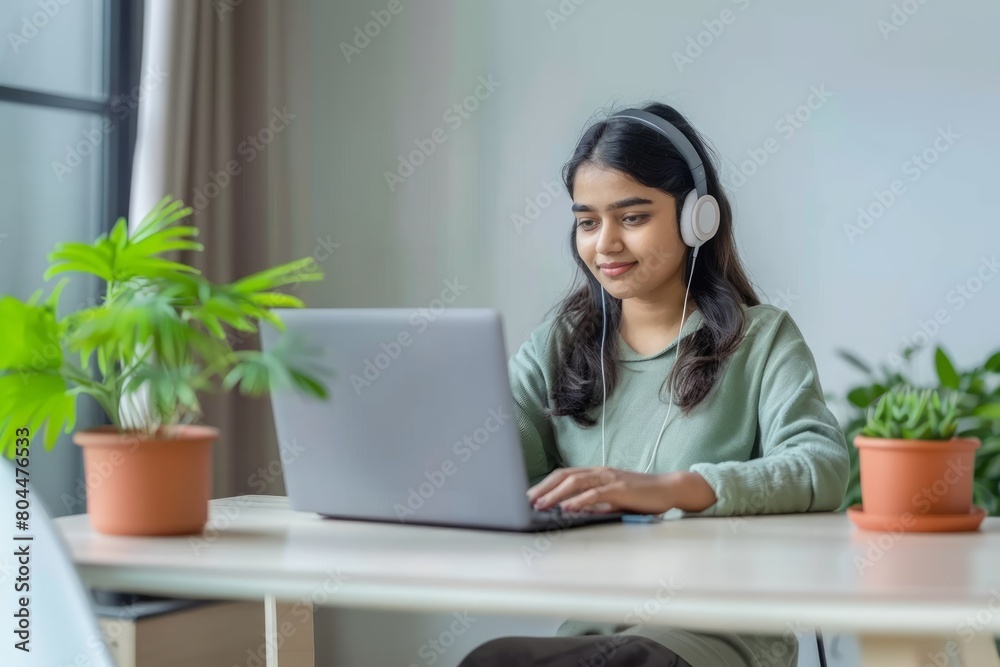 A young indian female student sitting at the table using headphones when studying A young indian female student sitting at the table using headphones when studying