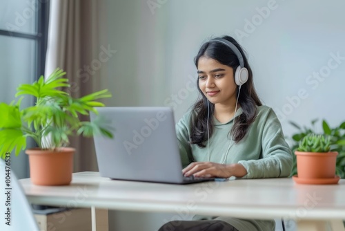 A young indian female student sitting at the table using headphones when studying © Ingenious Buddy 
