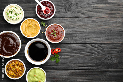 Different tasty sauces in bowls, parsley, chili pepper and rosemary on black wooden table, flat lay. Space for text