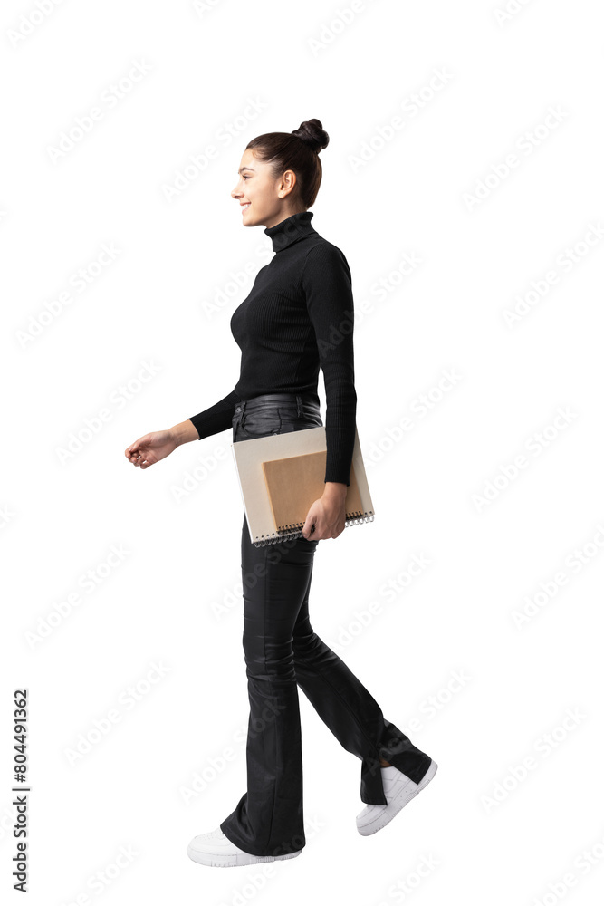 © Who is Danny - A woman walking profile view, holding a notebook, wearing black clothes, posed on a white background, depicting a concept of casual business attire