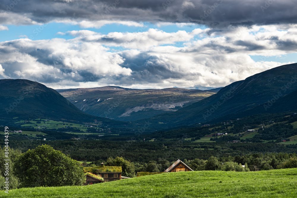 Obraz premium Evening falls over the serene Oppdal Valley in Norway, the farm roofs peaking just above the hillside and leading you further into the scene with mountains embracing the landscape