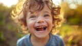 Close-up of a joyful toddler laughing joyfully, his curly hair backlit by golden sunlight