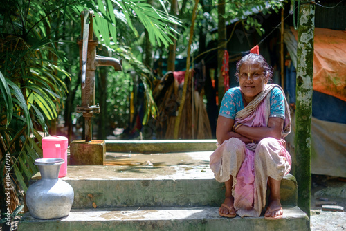 South asian elderly woman sitting beside a tube well wearing traditional dress 