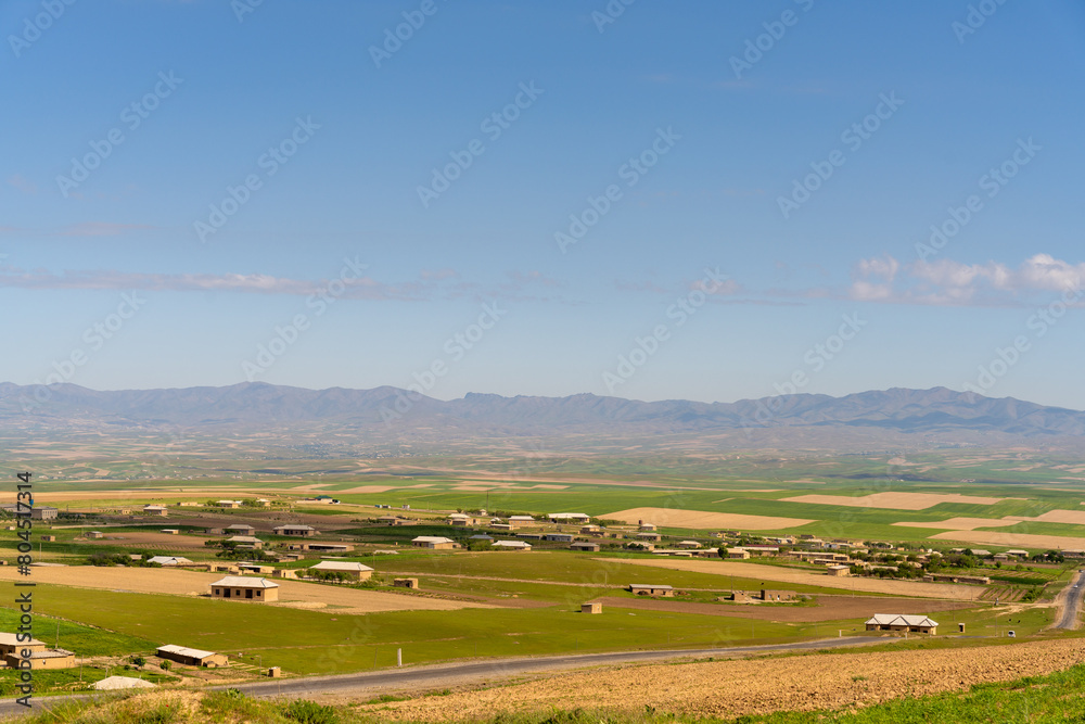 A rural landscape with a few houses and a road. The sky is clear and blue