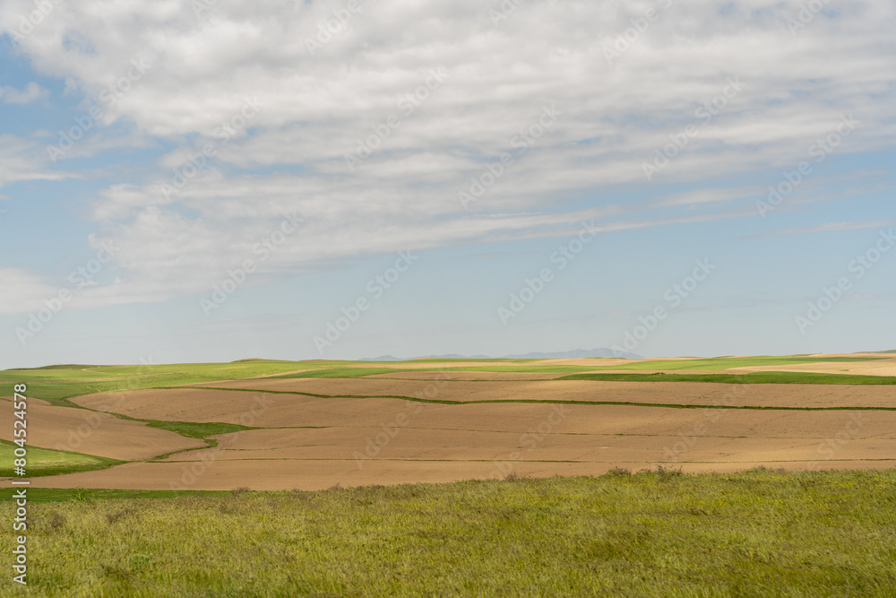 A large, empty field with a few clouds in the sky. The sky is blue and the sun is shining