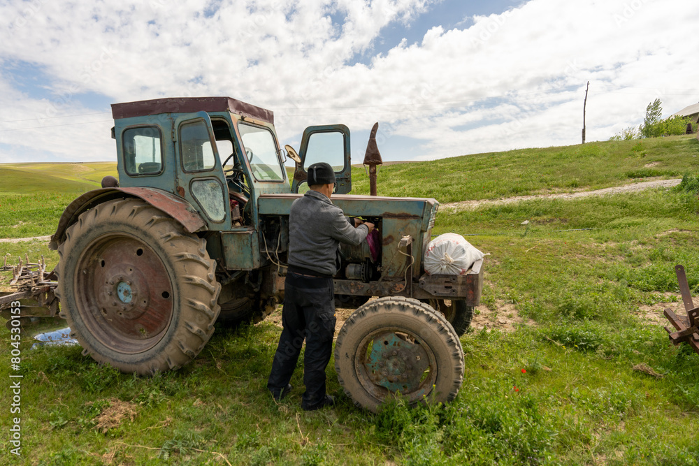 A man is working on an old tractor in a field. The tractor is old and rusty, and the man is trying to fix it. The scene is peaceful and quiet, with the man focused on his task A man is working on an old tractor in a field. The tractor is old and rusty, and the man is trying to fix it. The scene is peaceful and quiet, with the man focused on his task