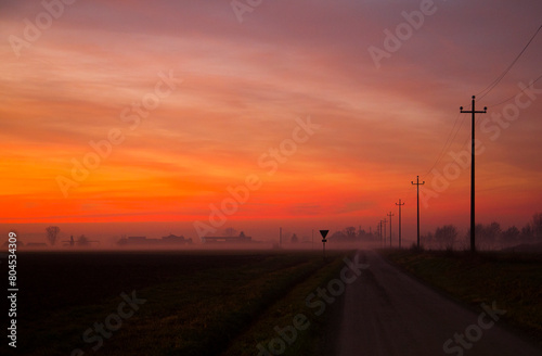 Afterglow of sunset over natural landscape with power lines and dirt road