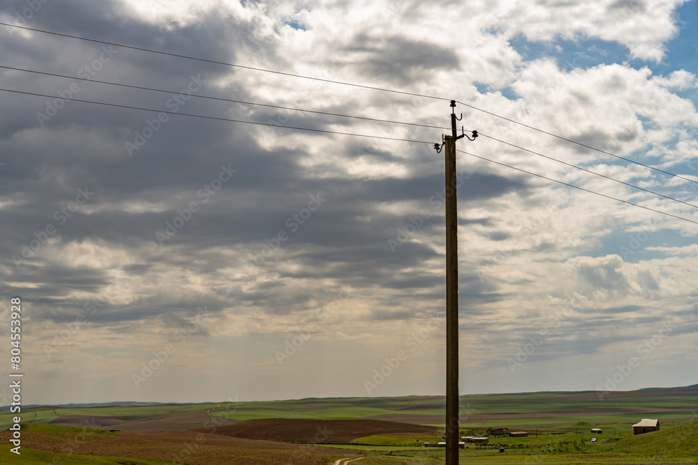 A tall power pole stands in a field with a cloudy sky above
