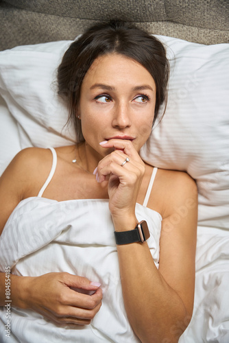 Top view of thoughtful attractive caucasian woman lying on bed and looking away
