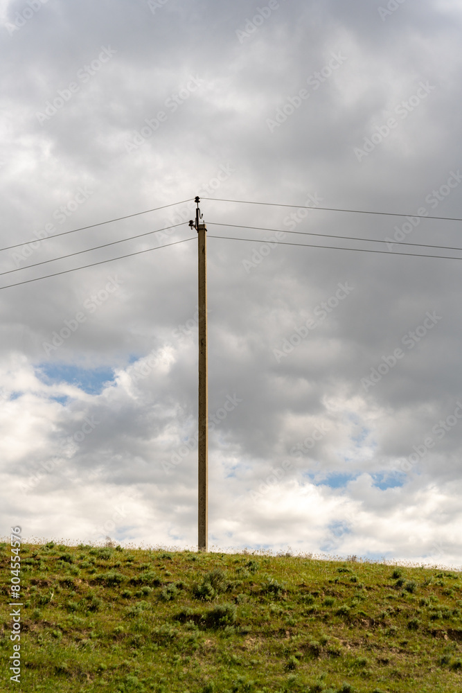 A tall pole with power lines on it stands in a field. The sky is cloudy and the grass is green