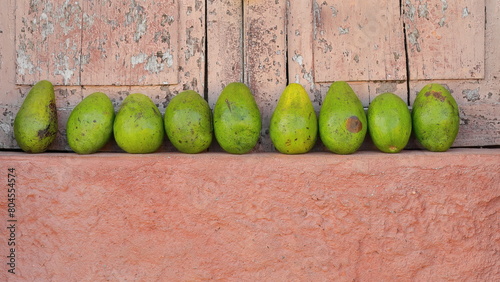 Line of green avocados, Catalina variety, on the salmon-orange ledge of a closed window, on a street next to Plaza Mayor Square. Trinidad-Cuba-226