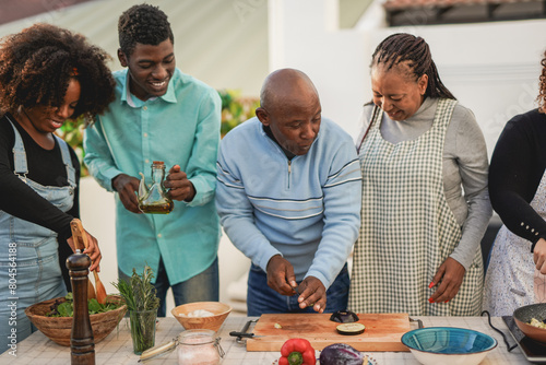 Happy african family cooking together healthy dinner at house patio - Parents and adult children preparing food outdoor