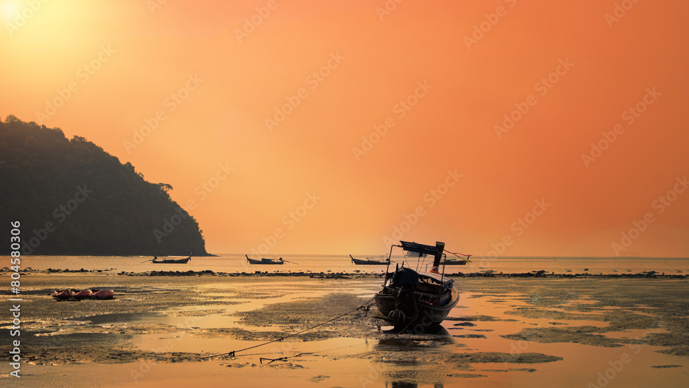 A view of a long-tail boat parked on the beach at dusk against the red sky. beautiful summer landscape Group of long-tail boats fishing in the Andaman Sea, Koh Lipe, Thailand's paradise island.