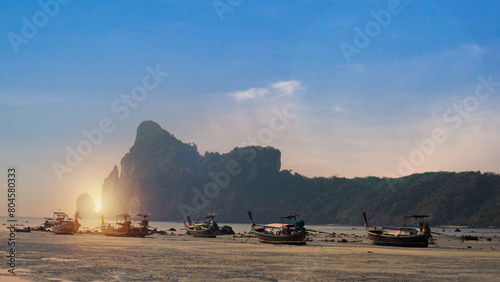 A view of long-tail boats lined up on the beach at dusk against the red sky. Stunning summer landscape Group of long-tail boats fishing in the Andaman Sea, Koh Lipe, Thailand's paradise island. photo