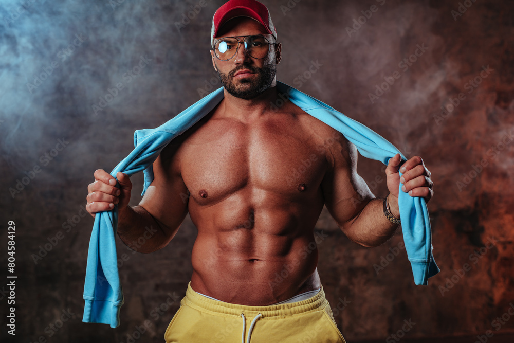 Obraz premium Young strong man bodybuilder in red cap on wall background