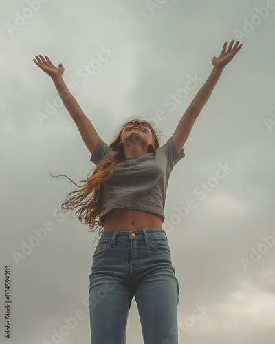 Photo d'une jeune femme en jean levant les bras, ciel gris en arrière plan, parfaite illustration de la liberté et de la jeunesse photo