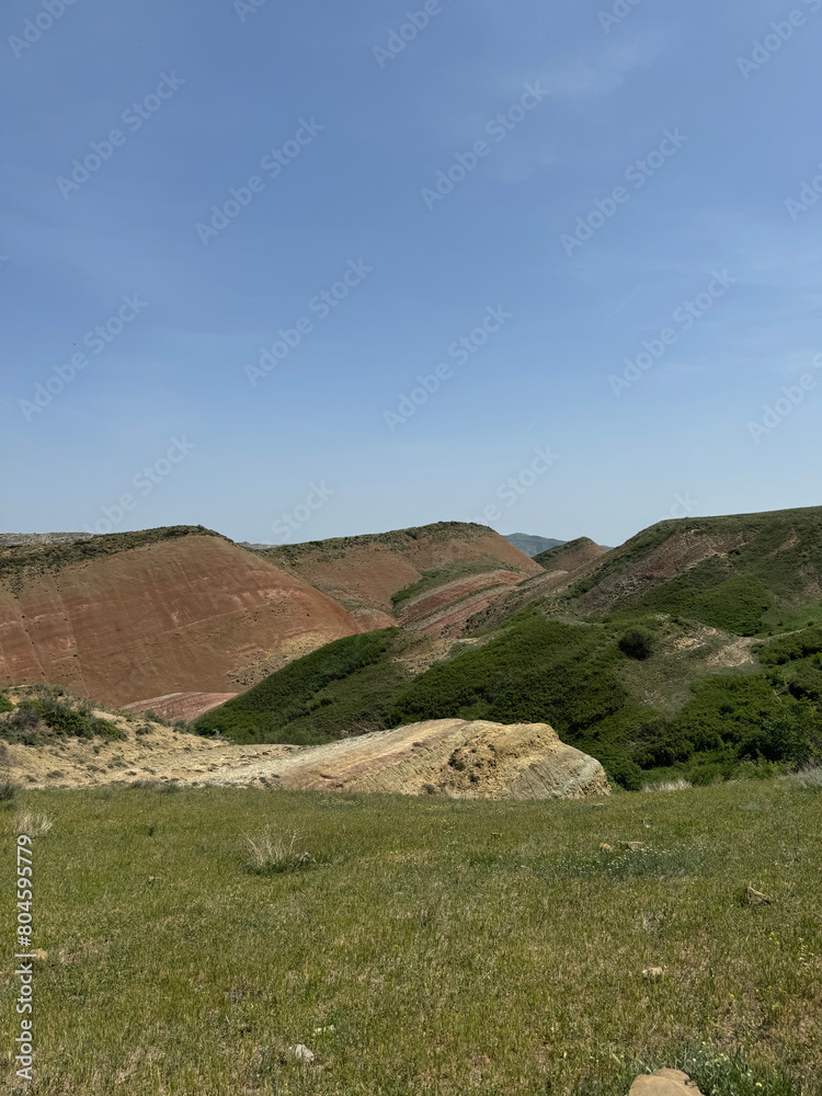 A green hillside with red mountains and a blue sky in David Gareja in Georgia A green hillside with red mountains and a blue sky in David Gareja in Georgia