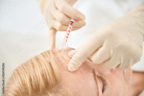 Close-up doctor making microinjections of filler to female client forehead photo