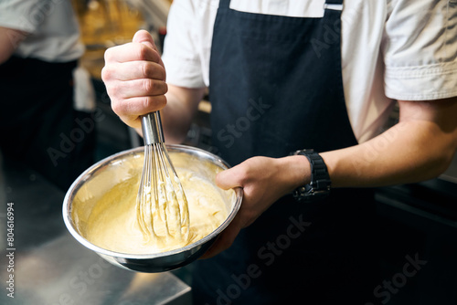 Cropped male chef mixing dough with whisk in bowl for cooking dish in restaurant photo