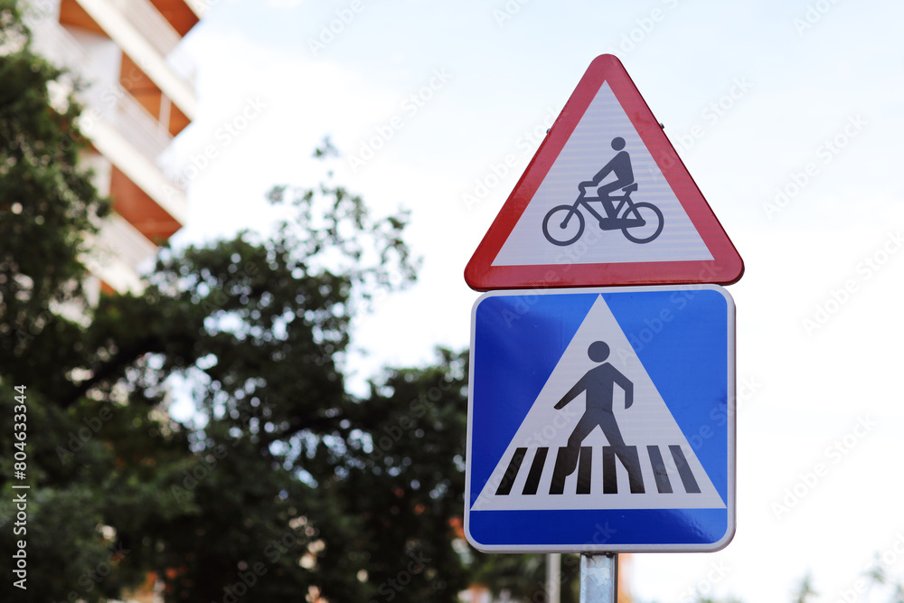 Warning red triangular bicycle sign above square pedestrian crossing sign outdoors on city street. Traffic safety regulations. Cyclists may appear, intersection with cycle path outside intersection Warning red triangular bicycle sign above square pedestrian crossing sign outdoors on city street. Traffic safety regulations. Cyclists may appear, intersection with cycle path outside intersection