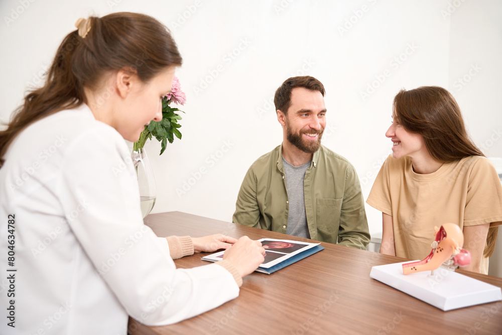 Doctor showing woman ultrasound scan of pregnant belly with twins to couple Doctor showing woman ultrasound scan of pregnant belly with twins to couple