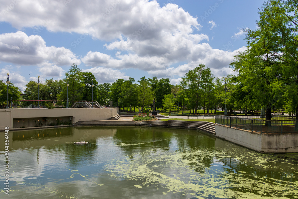Fototapeta premium a gorgeous spring landscape at Louis Armstrong Park with lush green trees, plants and grass, a lake, blue sky and clouds in New Orleans Louisiana USA