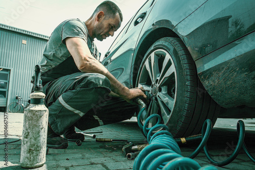 .A car service technician unscrews a wheel from a car using a pneumatic tool, close up view in overalls. photo