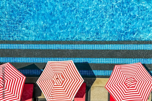 Red and white striped umbrellas along sparkling pool embody resort luxury, offering idyllic escape into leisure and visual delight, perfect for upscale summer vacation seekers. Flat lay, copy space photo