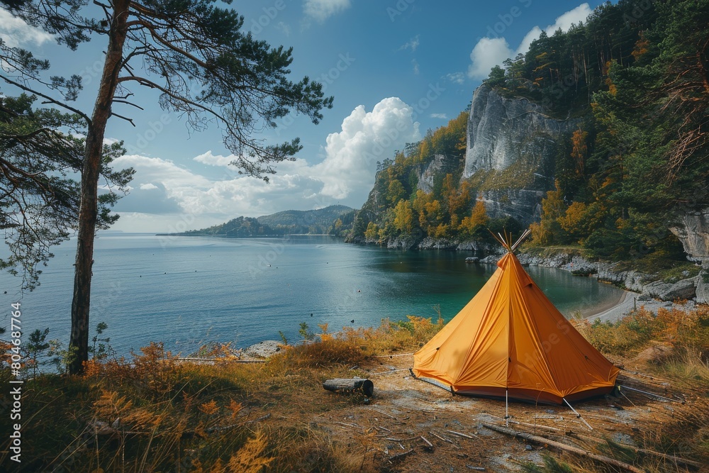 Obraz premium An isolated bright orange tent set up on a shore, overlooking a serene lake surrounded by autumnal forest and rocky cliffs