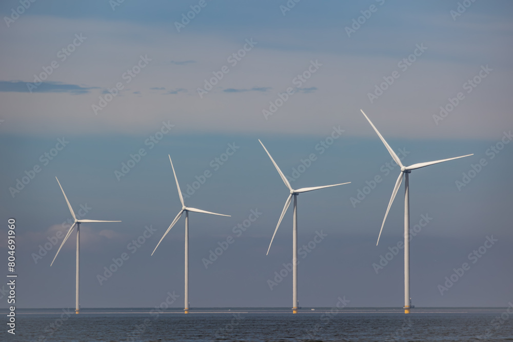 Wind farm of wind mills, generators, wind turbines, off shore in a sea or lake IJsselmeer in the Netherlands. Multiple tall windmills and rotor blades generating green sustainable energy, electricity Wind farm of wind mills, generators, wind turbines, off shore in a sea or lake IJsselmeer in the Netherlands. Multiple tall windmills and rotor blades generating green sustainable energy, electricity