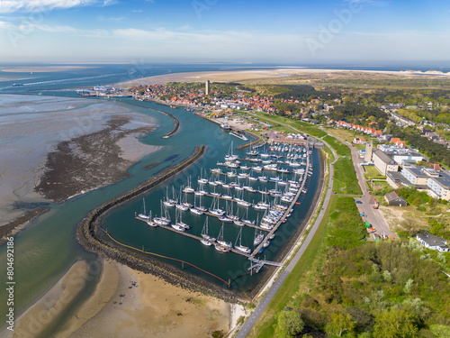 Aerial drone image of the historic Frisian town of West Terschelling on the Wad island in world heritage site Wadden Sea. Old brick lighthouse Brandaris and marina with dunes, sandbanks and tidal sea 