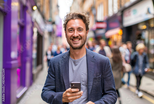 a happy man in his 30s smiles at the camera while holding his iphone on a purple background