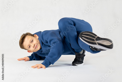 Boy in breakdancing position.Hip hop dance. Bboying basics. Boy in a blue tracksuit on a white background.Cheerful boy dancing breakdance photo