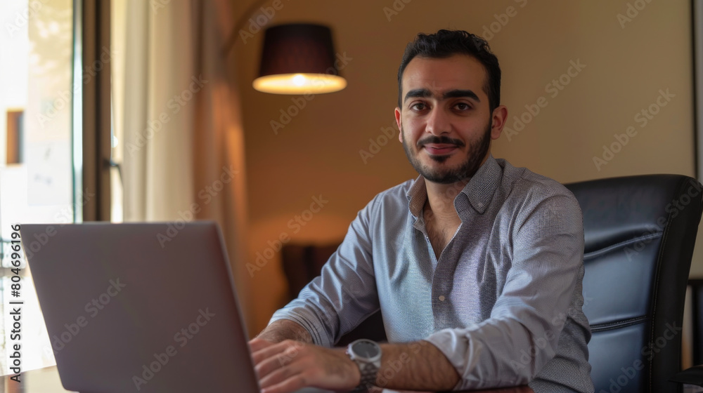Portrait of a young man working on a laptop in a home office. Happy Arab doing work remotely on a laptop computer. Freelancing concept. Portrait of a young man working on a laptop in a home office. Happy Arab doing work remotely on a laptop computer. Freelancing concept.