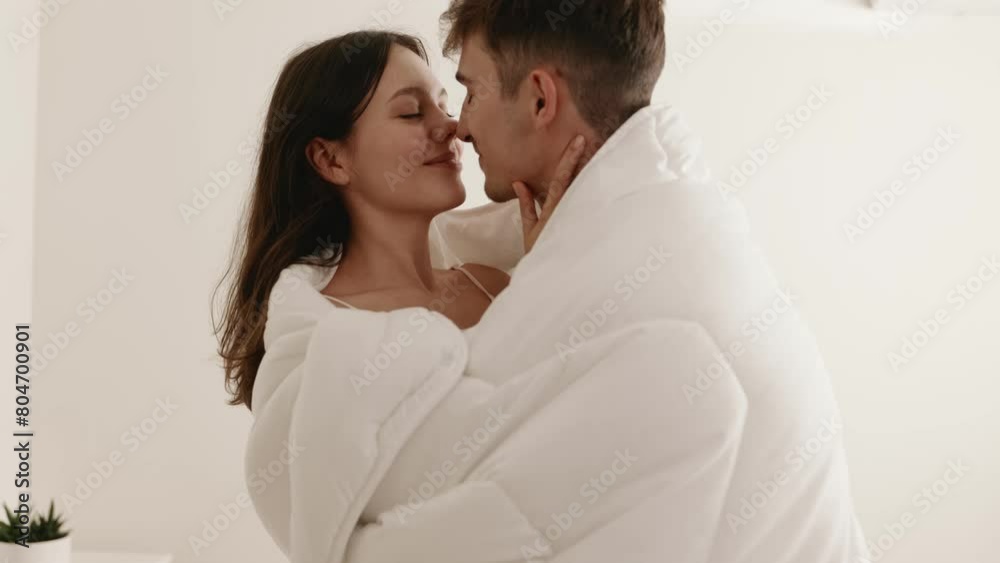 A young couple wrapped in a bed cover, embracing each other in a tender, loving gesture, embodying closeness and romance. A young couple wrapped in a bed cover, embracing each other in a tender, loving gesture, embodying closeness and romance.