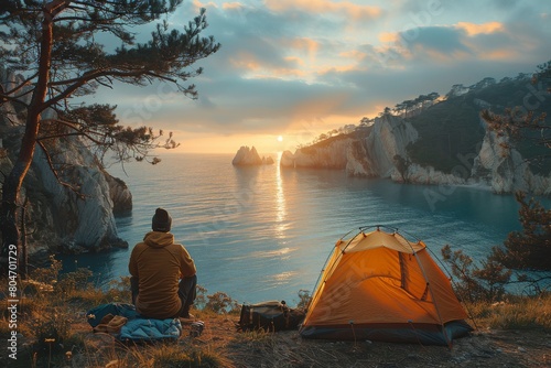 A person sitting beside an orange tent enjoying the sunset by the sea amidst rocky cliffs and pine trees