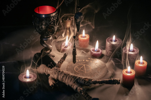Принти на полотні A haunting occult setup featuring a pendulum, mystical symbols, candles, a voodoo doll, and a ritual goblet amidst swirling smoke