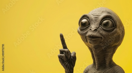 funny portrait of a grey alien pointing up on yellow copy space background