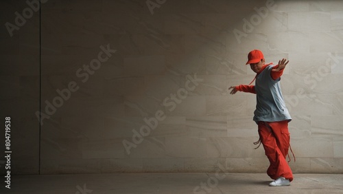 Handsome choreographer practice street dance in gray background. Young attractive b boy dancer perform while wearing stylish cloth. Feeling of lively step. Copy space. Outdoor sport 2024. Sprightly.