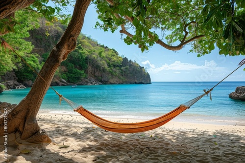 An inviting orange hammock hangs under leafy branches on a beautiful sandy beach with clear blue waters
